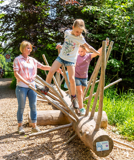 Kinder auf einem Holzstrunk am spielen, auf dem Zugiblubbi Erlebnisweg